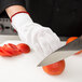 A person wearing Victorinox cut resistant gloves cutting a tomato on a counter.