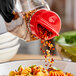 A person using a red 53/485 dual flapper spice lid to sprinkle seasoning onto a bowl of pasta.