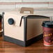 A cardboard box with a lid from Sabert with two coffee cups on a table.