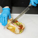 A person wearing blue gloves cutting a sandwich with a Dexter-Russell V-Lo scalloped bread and sandwich knife.