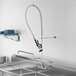 A stainless steel sink with a Regency wall-mounted pre-rinse faucet and double-jointed hose.