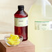 A jug of LorAnn Oils Lemonade Natural Flavor on a counter next to a bowl of lemons.