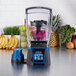 A Waring commercial blender with a blue lid and container filled with kale and fruit.