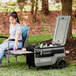 A woman sitting in a lawn chair with an Igloo Trailmate Journey cooler on a table.