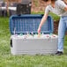 A woman opening an Igloo cooler filled with bottles on a table outdoors.