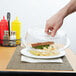 A hand reaching for a sandwich on a clear plate with a Cambro clear plate cover.