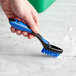 A hand holding a blue Lavex grout brush with a green and black device.