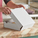 A person opening a white corrugated bakery box with a lid