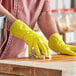 A person wearing Lavex yellow latex gloves cleaning a wooden surface.