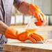 A man wearing Lavex orange dishwashing gloves cleaning a cutting board on a counter.