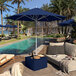 A pool with wooden chairs and a blue California Umbrella over them.