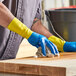A man wearing blue and yellow Lavex rubber gloves cleaning a wooden surface.