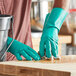 A person wearing Lavex green rubber gloves cleaning a wooden surface.