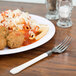 A WNA Comet Reflections Duet plastic fork with an ivory handle next to a plate of pasta and meatballs.