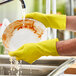A person wearing yellow Lavex latex gloves washes a plate.