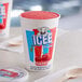 A close up of an ICEE Cherry Freeze cup filled with ice cream with a wooden spoon on a white towel.
