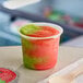 A Luigi's Strawberry Kiwi Sorbet cup filled with frozen dessert with a spoon on top.