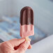 A person's hand holding a JonnyPops chocolate-dipped cherry popsicle.