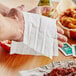 A hand using a Choice lemon scented moist towelette to clean chicken wings off a table.