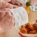 A person using a Choice 70% Alcohol Antiseptic Moist Towelette to grab a chicken wing from a basket.