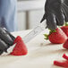 A person wearing black gloves uses a Victorinox utility knife to cut a strawberry.