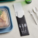 A black paper cutlery caddy with a fork and spoon inside.