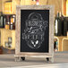 A Flash Furniture Canterbury weathered chalkboard with metal scrolled legs on a wood shelf with a business lunch sign.