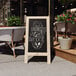 A Flash Furniture Canterbury weathered wood A-frame chalkboard with a sign on a sidewalk.