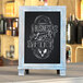 A Flash Furniture Canterbury rustic blue magnetic tabletop chalkboard with a lunch menu written on it.