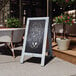 A Flash Furniture Canterbury Vintage Blue Wood A-Frame Chalkboard sign outside of a restaurant.