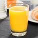 A Libbey juice glass filled with orange juice on a table in a breakfast diner.