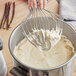 A hand holding a whisk whipping Violife plant-based heavy cream in a bowl.