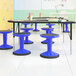 A group of Flash Furniture blue adjustable stools on a table in a classroom.