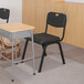 A black Flash Furniture Hercules plastic chair next to a school desk.