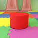 A red round ottoman on a colorful floor.