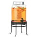 A Cal-Mil black glass beverage dispenser with an ice chamber on a metal stand filled with liquid and fruit.