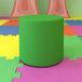 A green flexible seating circle modular ottoman on a colorful surface.
