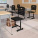 A black Flash Furniture Nila classroom chair next to a desk with a bag underneath it.