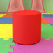 A red Flash Furniture Nicholas flexible seating circle ottoman on a colorful rug.