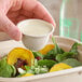 A person using a World Centric compostable portion cup to dip dressing on a salad.