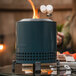 A woman roasts marshmallows over a Solo Stove Mesa XL Blue Tabletop Fire Pit on an outdoor patio table.