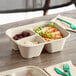 A World Centric compostable fiber container tray with three compartments filled with food on a table.