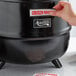 A hand putting a sticker on a black Avantco soup kettle.