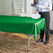 A woman standing next to a table with a green plastic table cover over it.