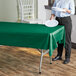 A woman standing next to a table with a Hunter Green plastic table cover.