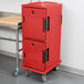 A red plastic Cambro Ultra Camcart food pan carrier with black handles on wheels.