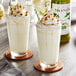 Two glasses of Monin Pistachio milkshakes with whipped cream and straws on a white background.