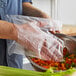 A hand in a Pak-Sher clear plastic glove holding a plastic bag over a bowl of chopped vegetables.