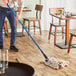 A man using a Lavex natural cotton looped end wet mop to clean a floor.