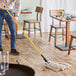 A person using a Lavex Natural Cotton Cut End Wet Mop with a yellow jaw-style mop handle to mop a wood floor.